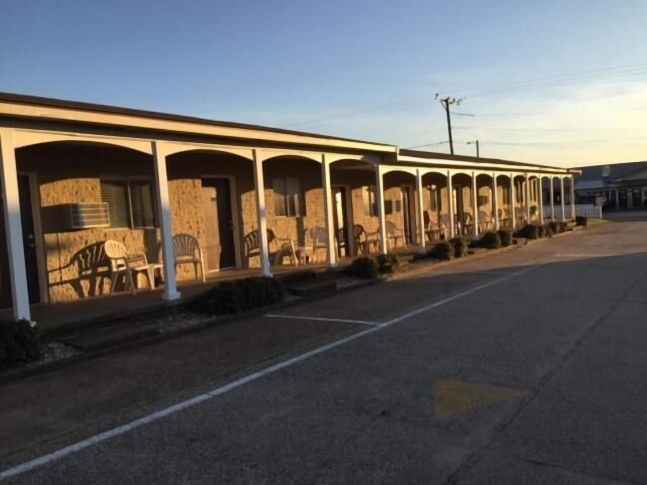 A motel with multiple rooms, each with a porch and chairs.