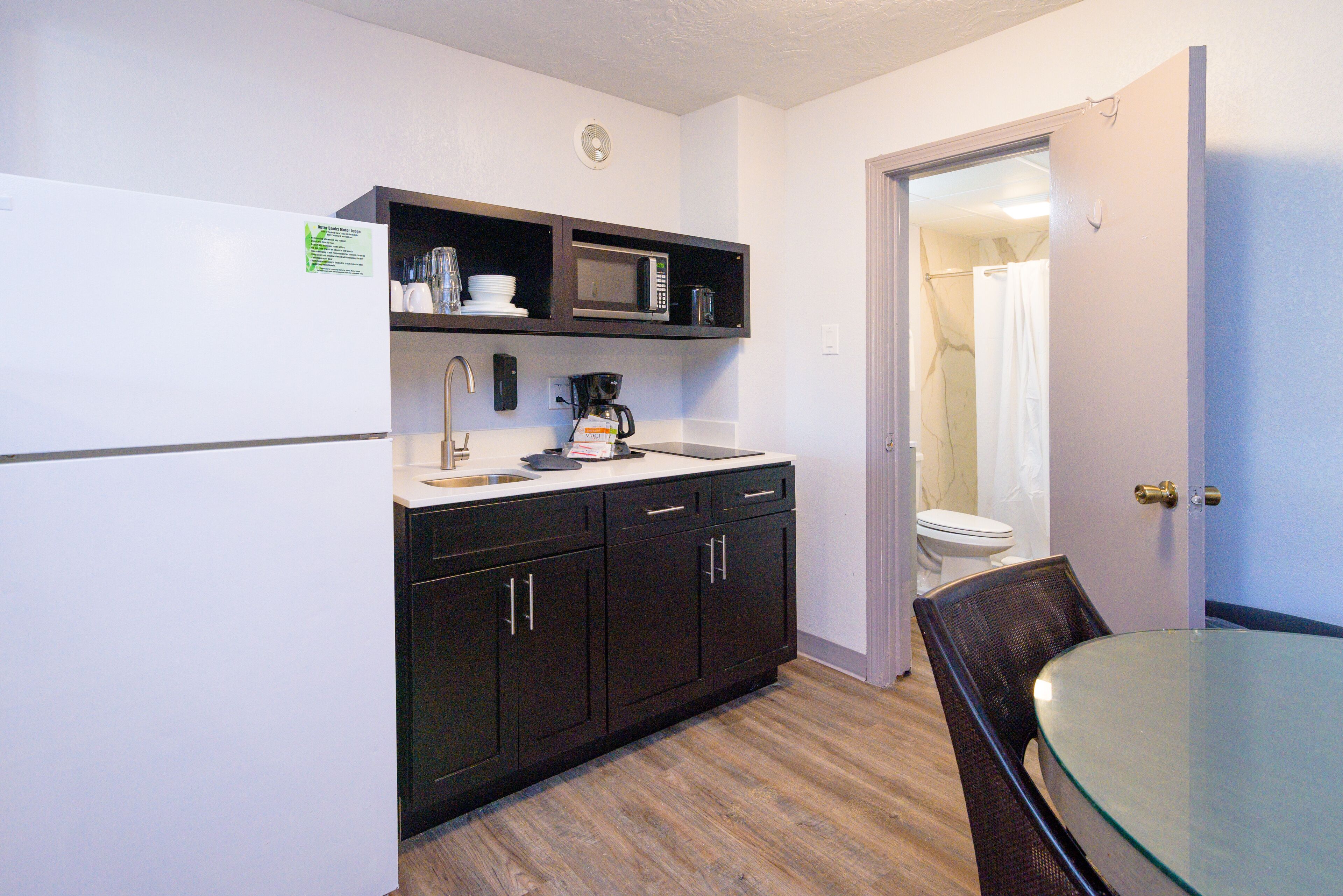 A compact kitchen with dark cabinets, a microwave, a coffee maker, and a glass table.