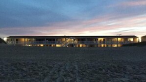 A beachfront hotel with multiple floors and balconies, featuring a series of windows and doors. - Outer Banks Motor Lodge (Kill Devil Hills)