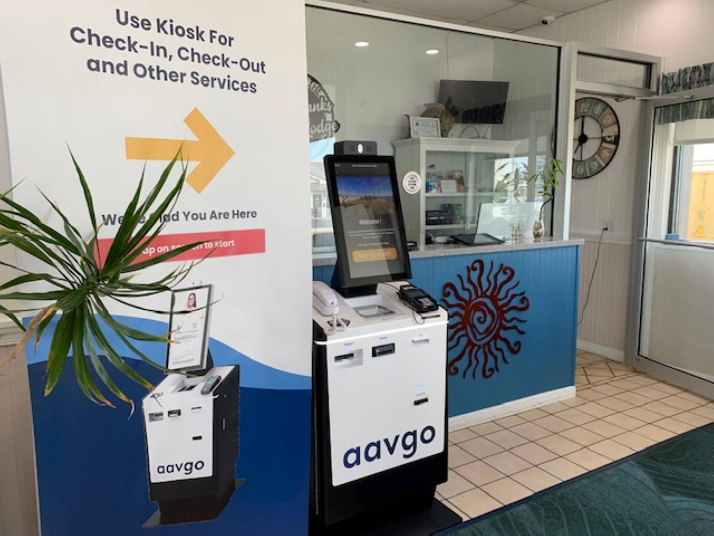 A kiosk with a sign for check-in and other services, a computer monitor, and a plant.