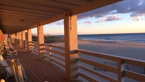 A wooden deck with chairs and a railing overlooking a beach. - Outer Banks Motor Lodge (Kill Devil Hills)