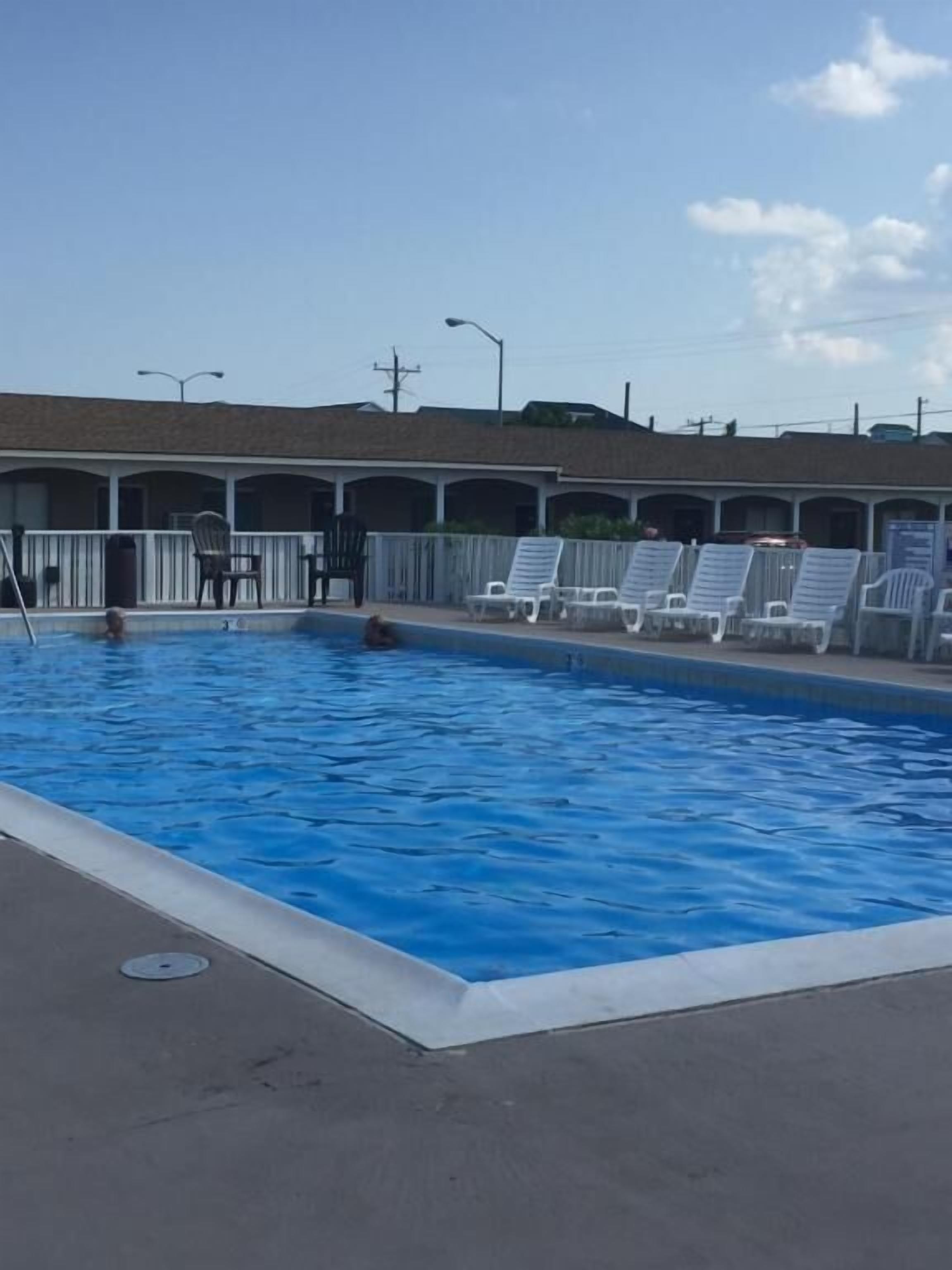 A swimming pool with lounge chairs and a building with multiple rooms in the background.
