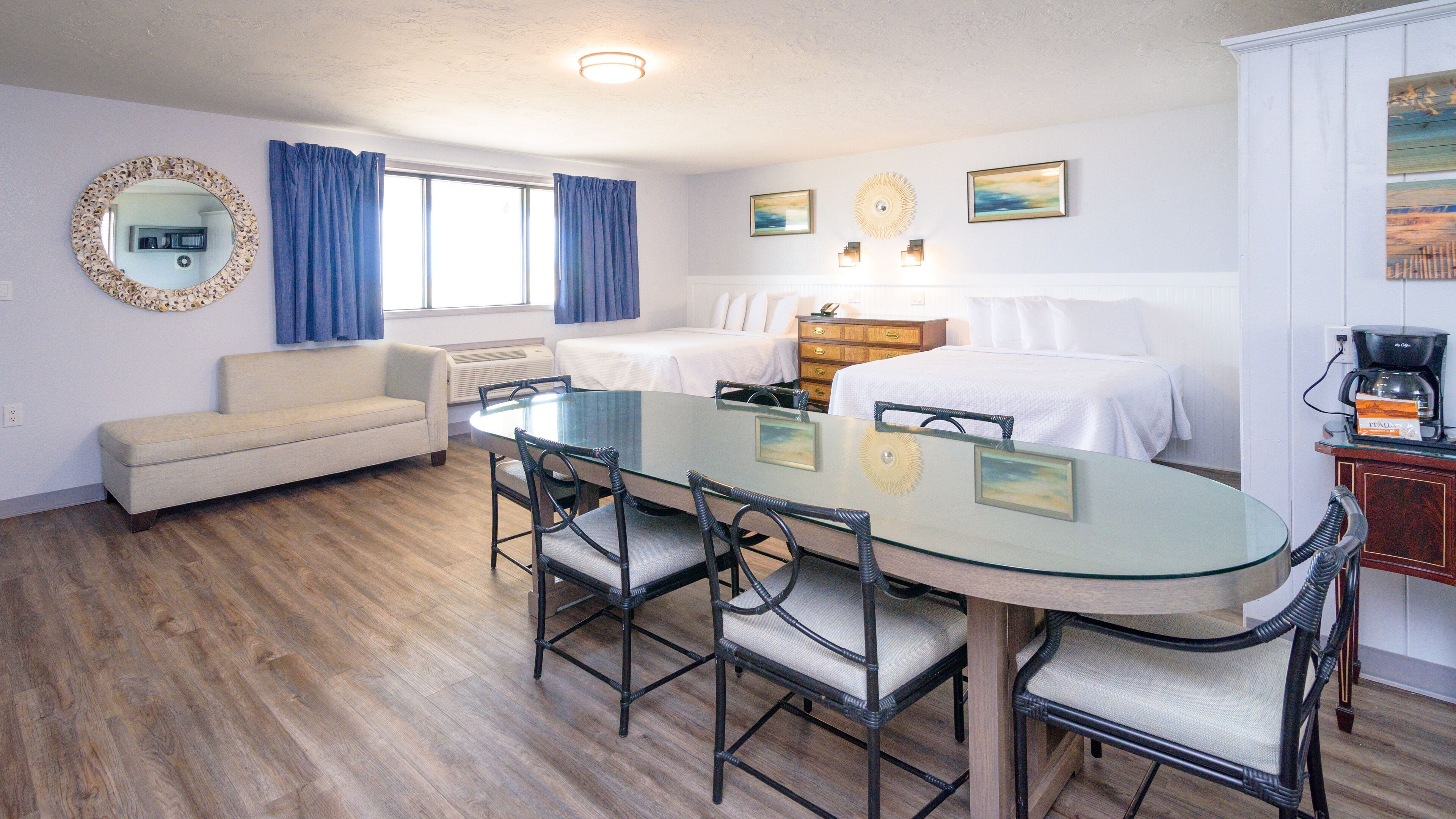 A hotel room with a dining area, a bed, a sofa, and a coffee machine.