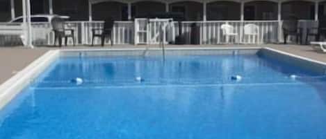 A swimming pool with a covered seating area and a building in the background.