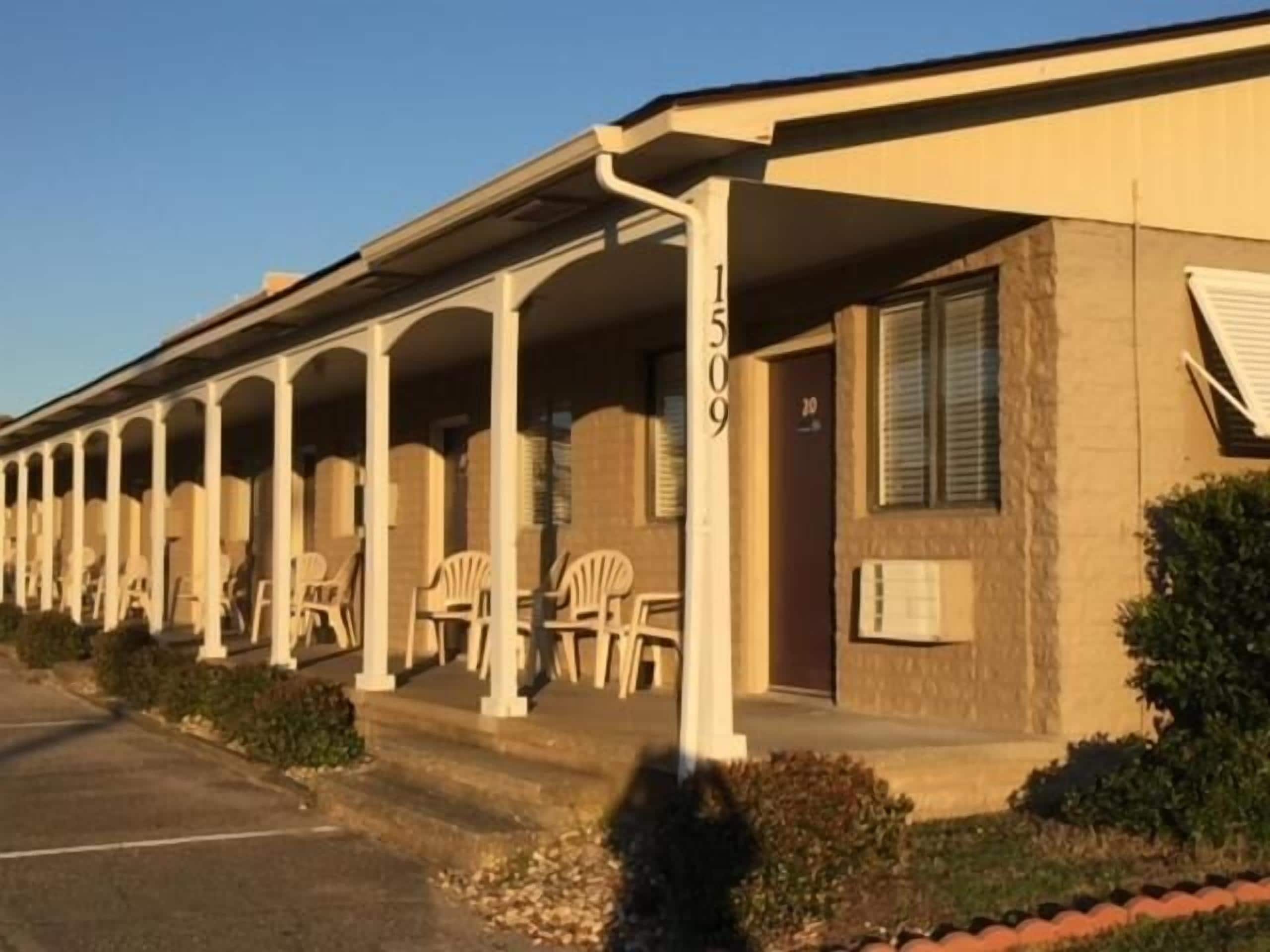 A motel with a row of single-story buildings, each with a covered porch and a number sign above the entrance.