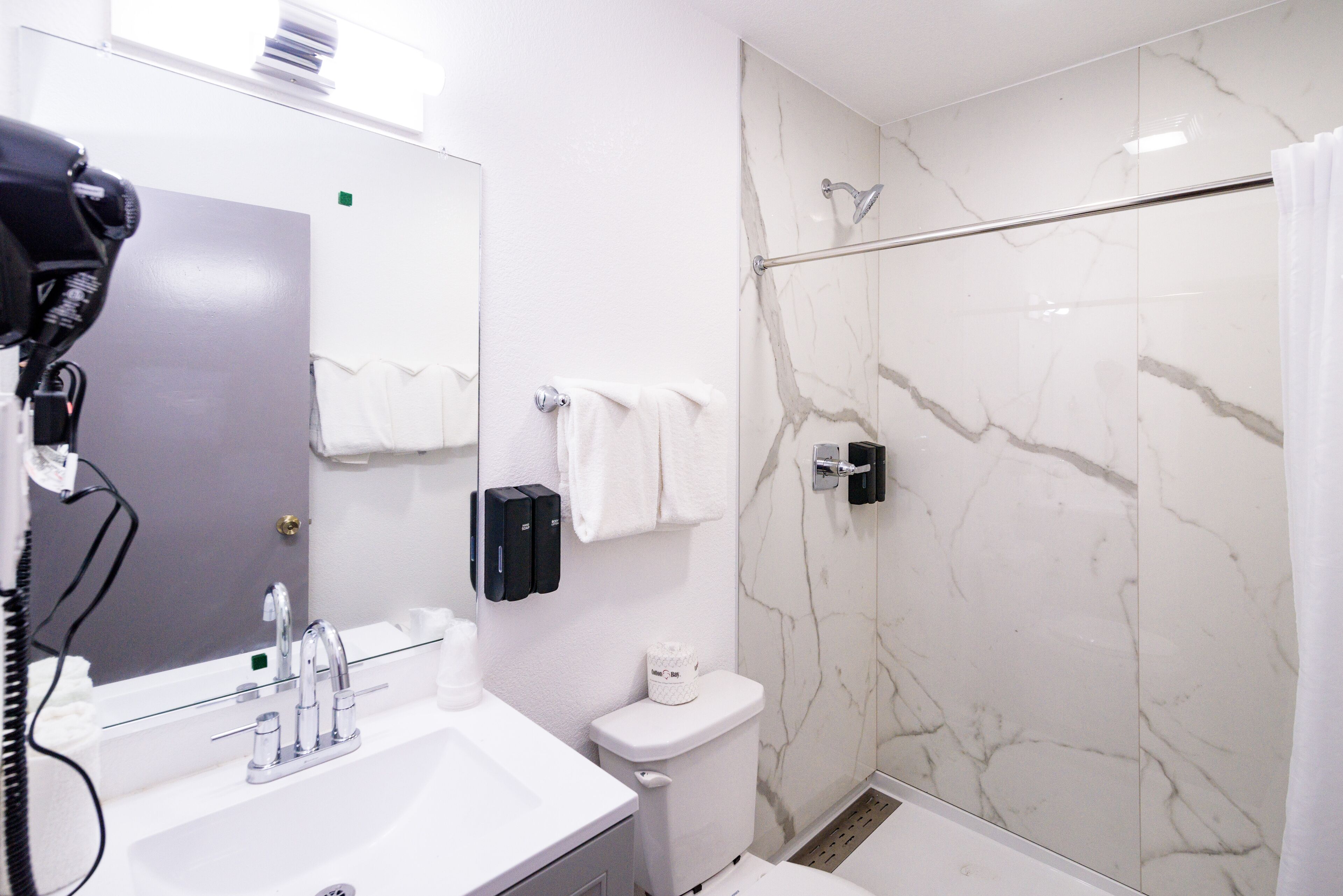A modern bathroom with a white sink, mirror, and toilet. It includes a glass shower enclosure and a towel rack.