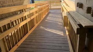 A wooden deck with railings, leading to a building with stone walls.