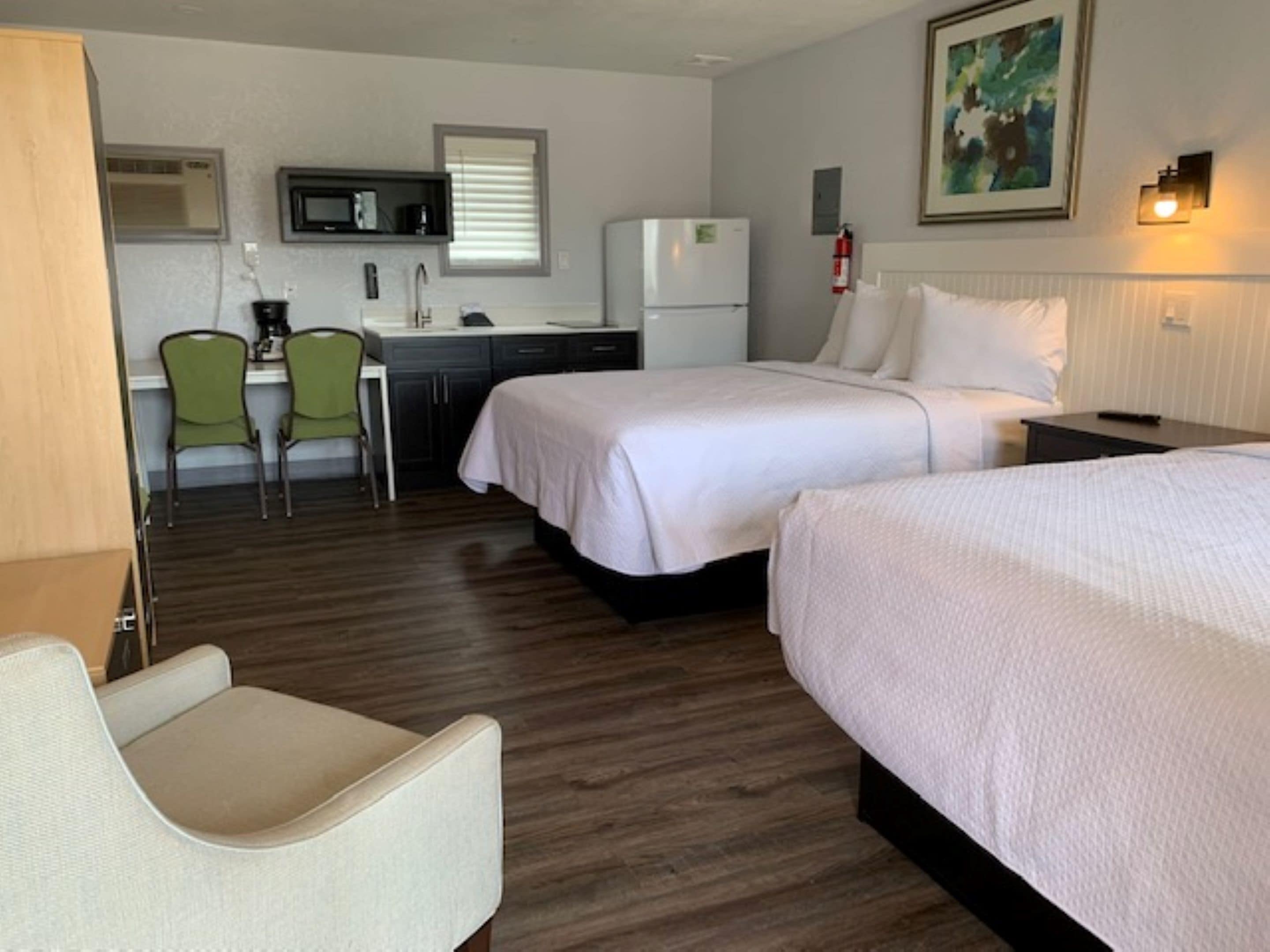A hotel room with two beds, a kitchenette, a dining area with a chair, and a small table.