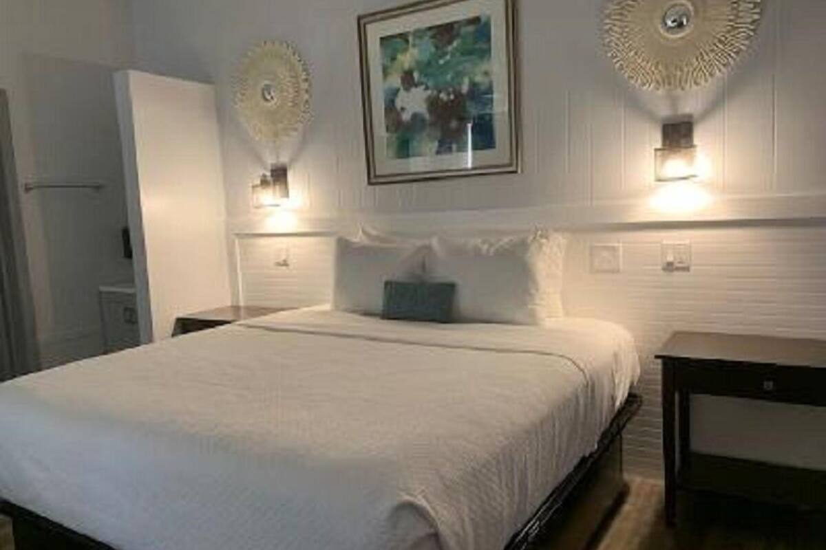 A neatly made bed with a white comforter and pillows, a bedside table, and a wall-mounted light fixture.