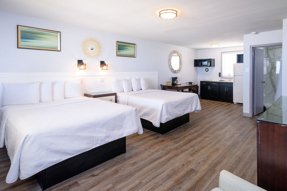 A hotel room with two beds, a small kitchen area, and a bathroom visible through an open door.
