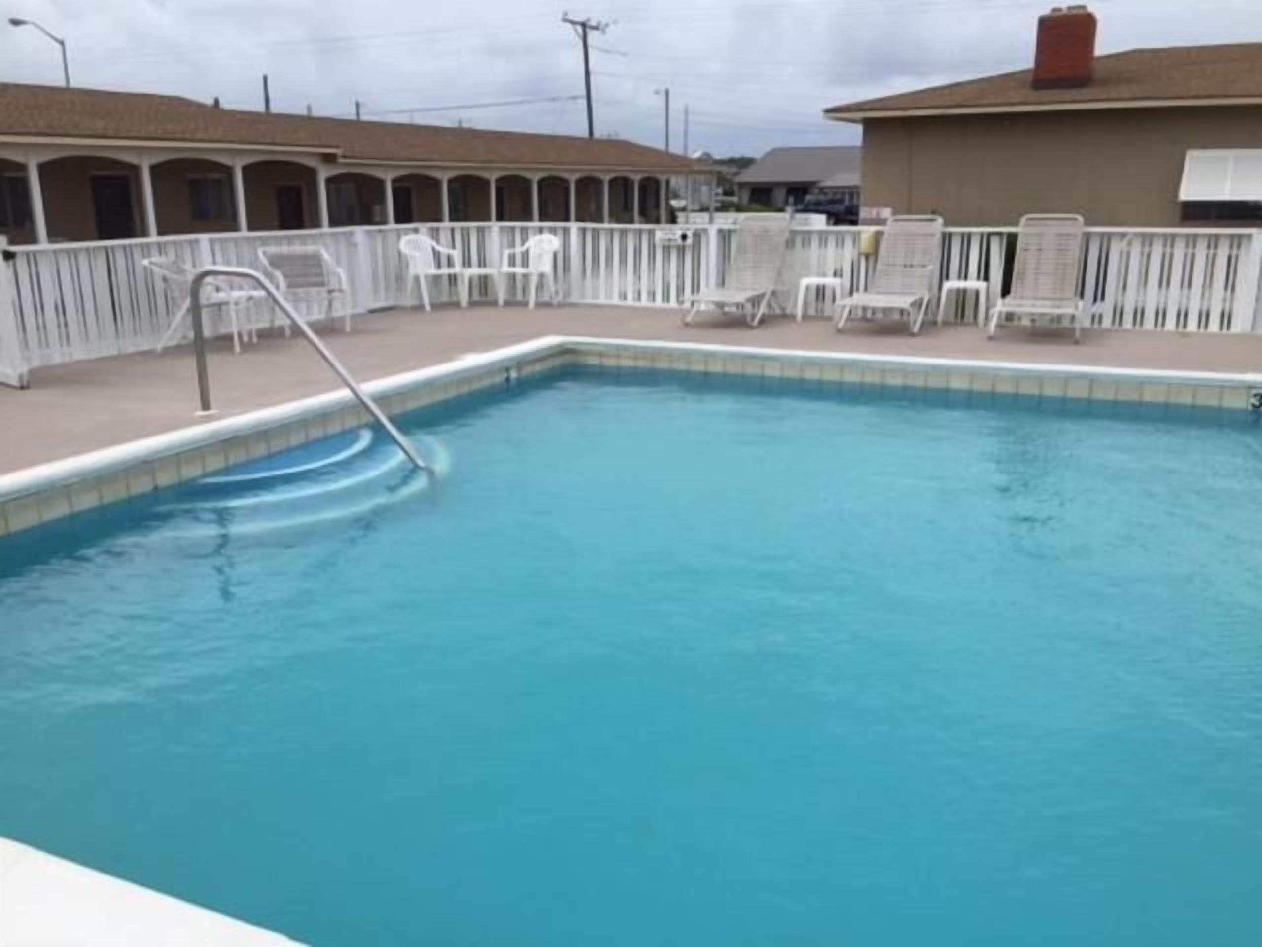 A swimming pool with a white deck and lounge chairs.