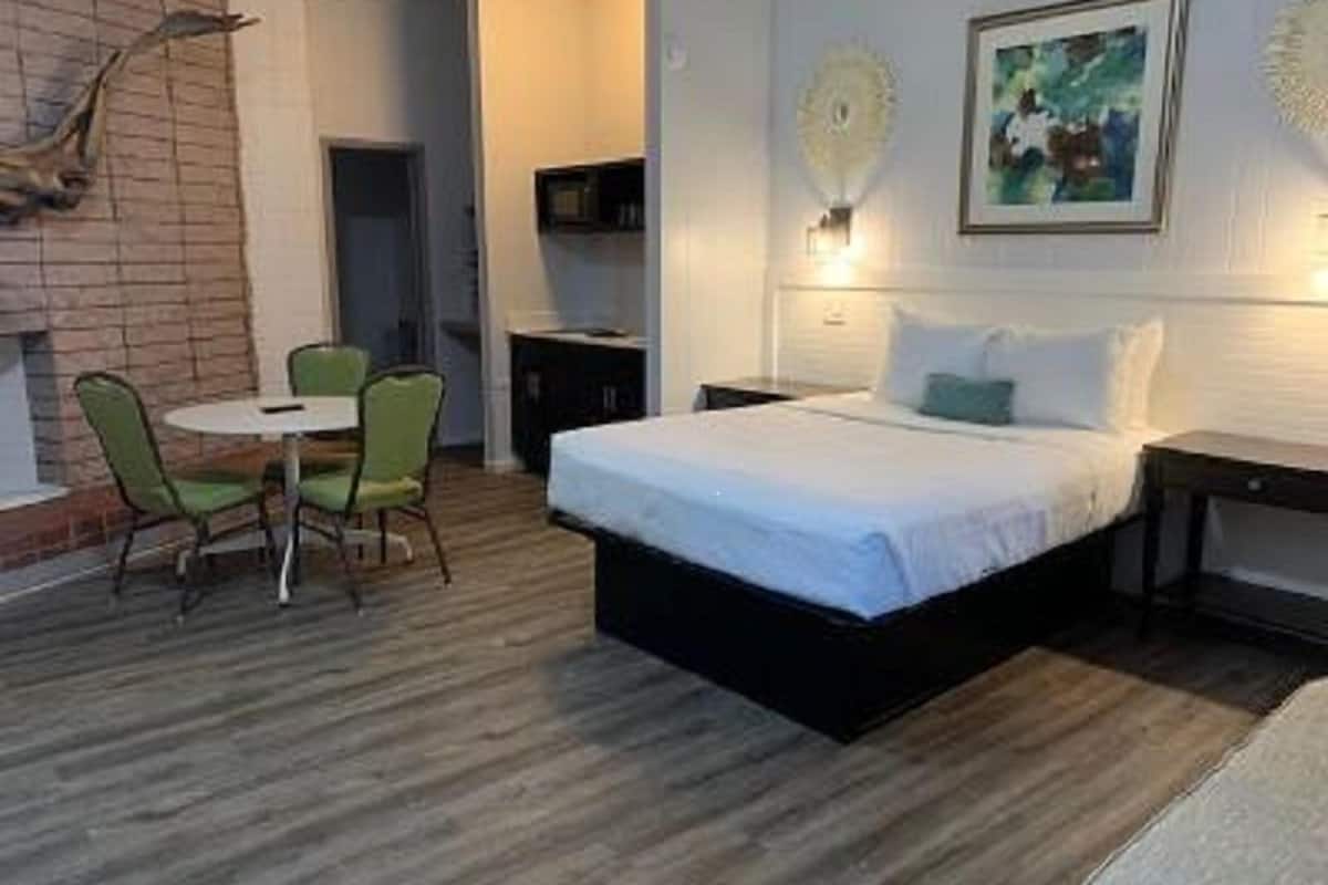 A bedroom with a bed, a small table, two chairs, a TV, and a decorative wall piece.