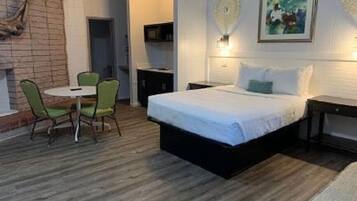Un dormitorio con cama, una mesita, dos sillas, un televisor y un adorno en la pared.