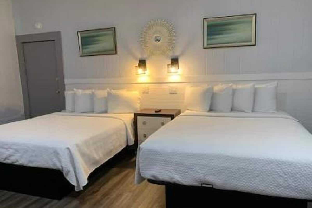 A hotel room with two single beds, a nightstand, a wall-mounted light fixture, and two framed pictures.