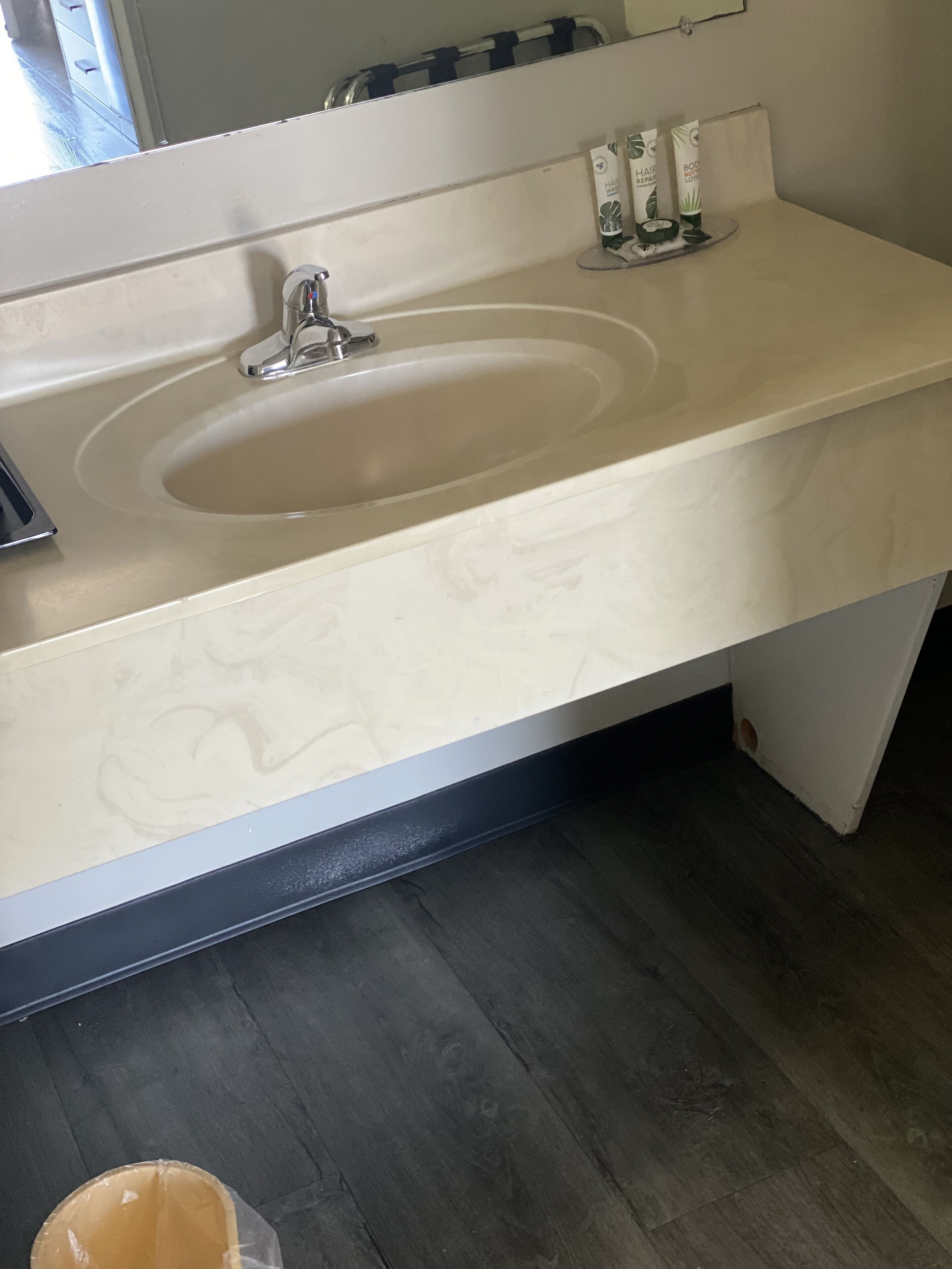 A bathroom with a beige sink, a mirror above it, and a dark wooden floor.
