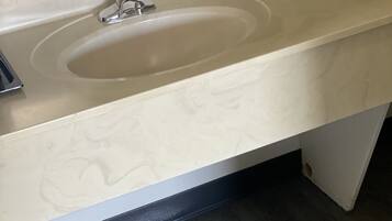 A bathroom with a beige sink, a mirror above it, and a dark wooden floor.