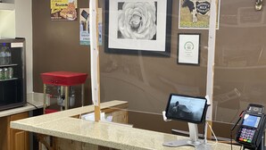Ein Tresen mit Zahlungsgerät, ein gerahmtes Bild von einer Blume und verschiedene Plakate an der Wand.