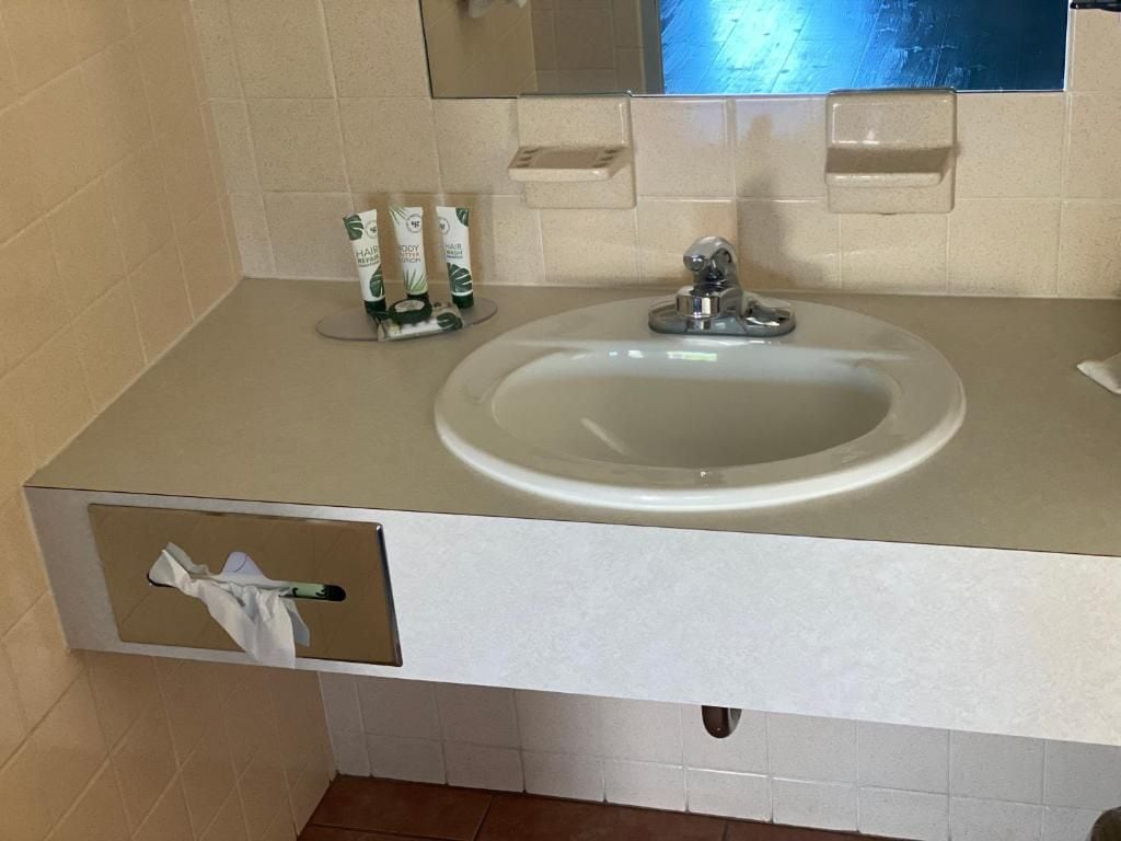 A bathroom sink with a mirror above it, a towel dispenser, and a tissue box.