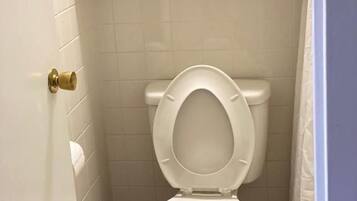 Un baño con inodoro, estante con artículos de aseo y toallero.