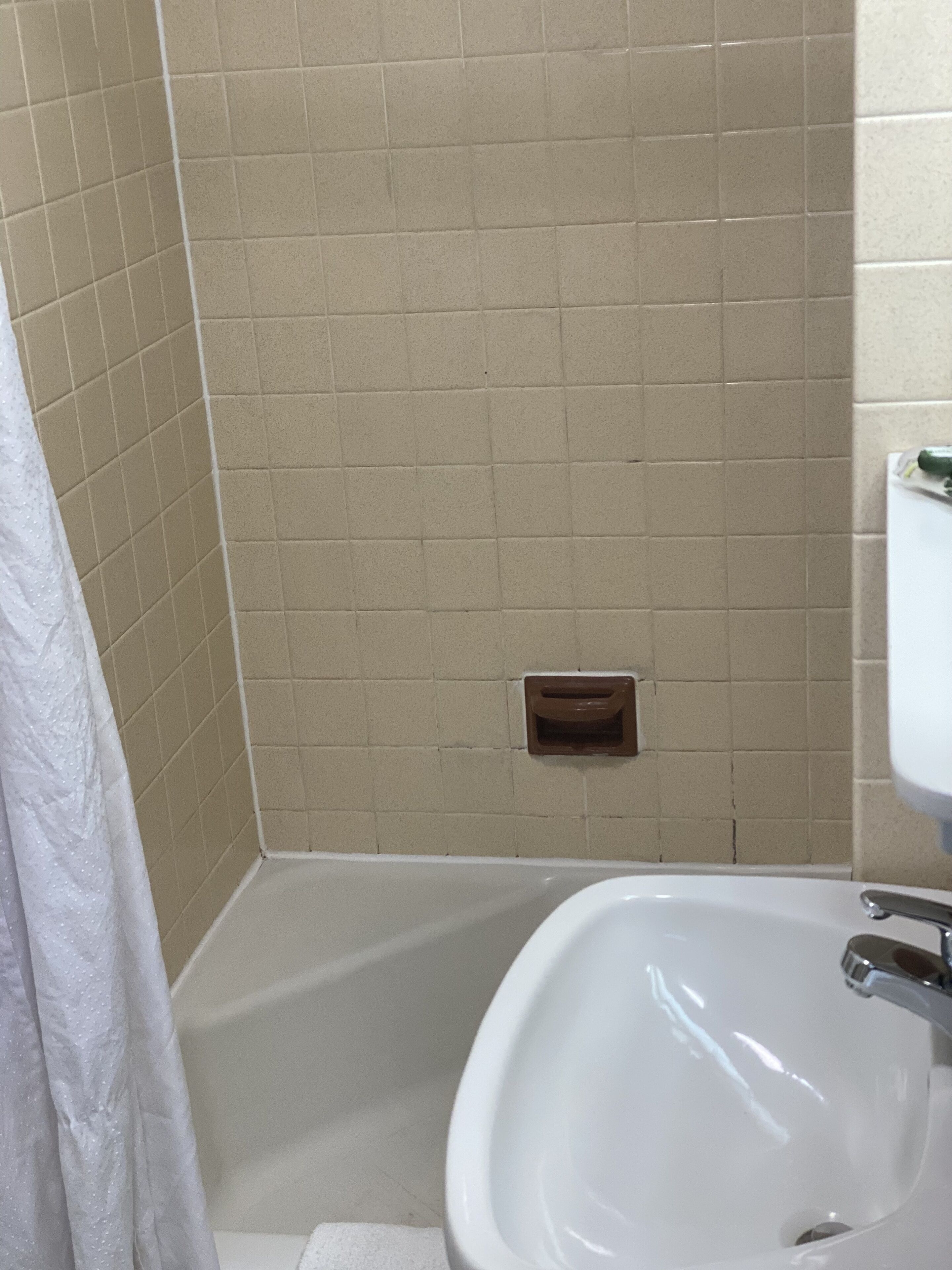 A bathroom with beige tiled walls, a white bathtub, and a white sink.