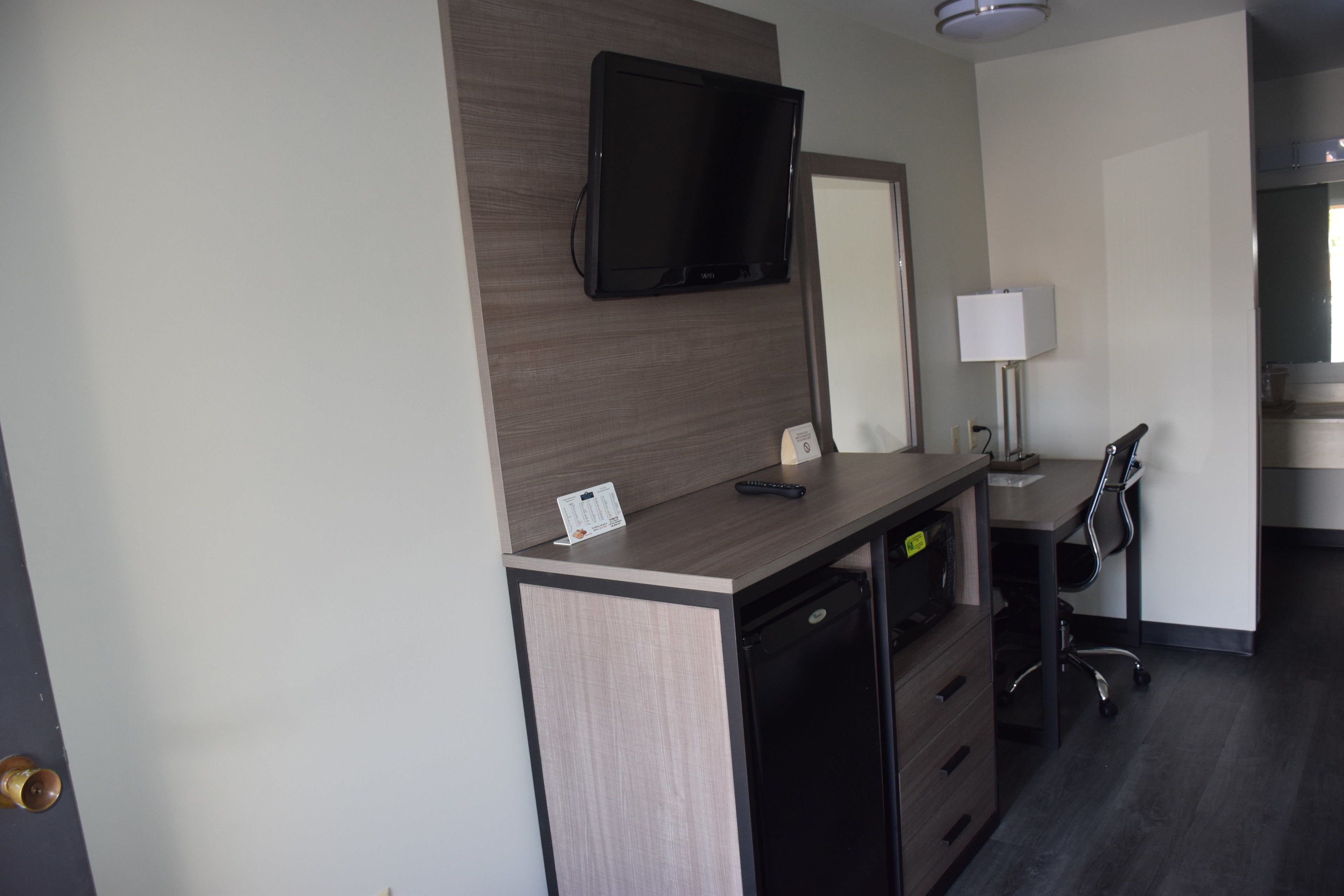 Une chambre d’hôtel équipée d’un bureau, d’un téléviseur fixé au mur, d’une lampe et d’une chaise.