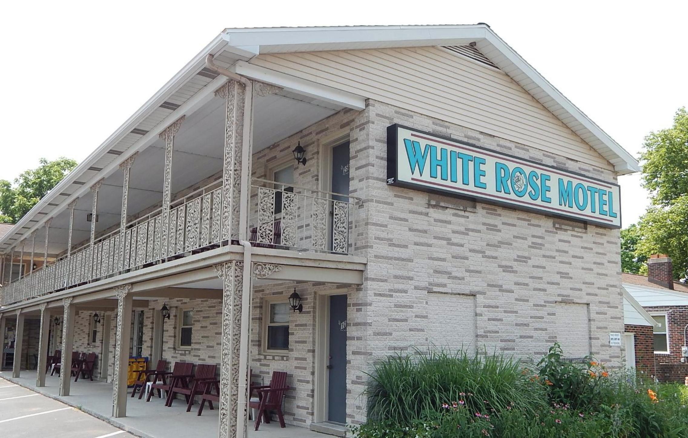 Un edificio a due piani con un balcone e un cartello con scritto 'WHITE ROSE MOTEL'.