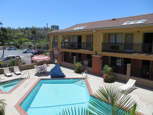 A hotel with a swimming pool, outdoor seating, and a parking lot.