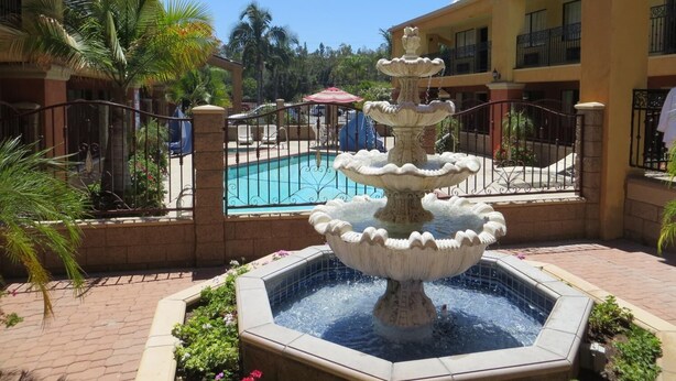 A multi-tiered fountain in a courtyard with a pool and a building in the background. - Azusa INN Motel (La Puente)