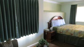 Quarto de hotel com uma cama, mesa de cabeceira com telefone, pequena mesa com planta e um sofá.