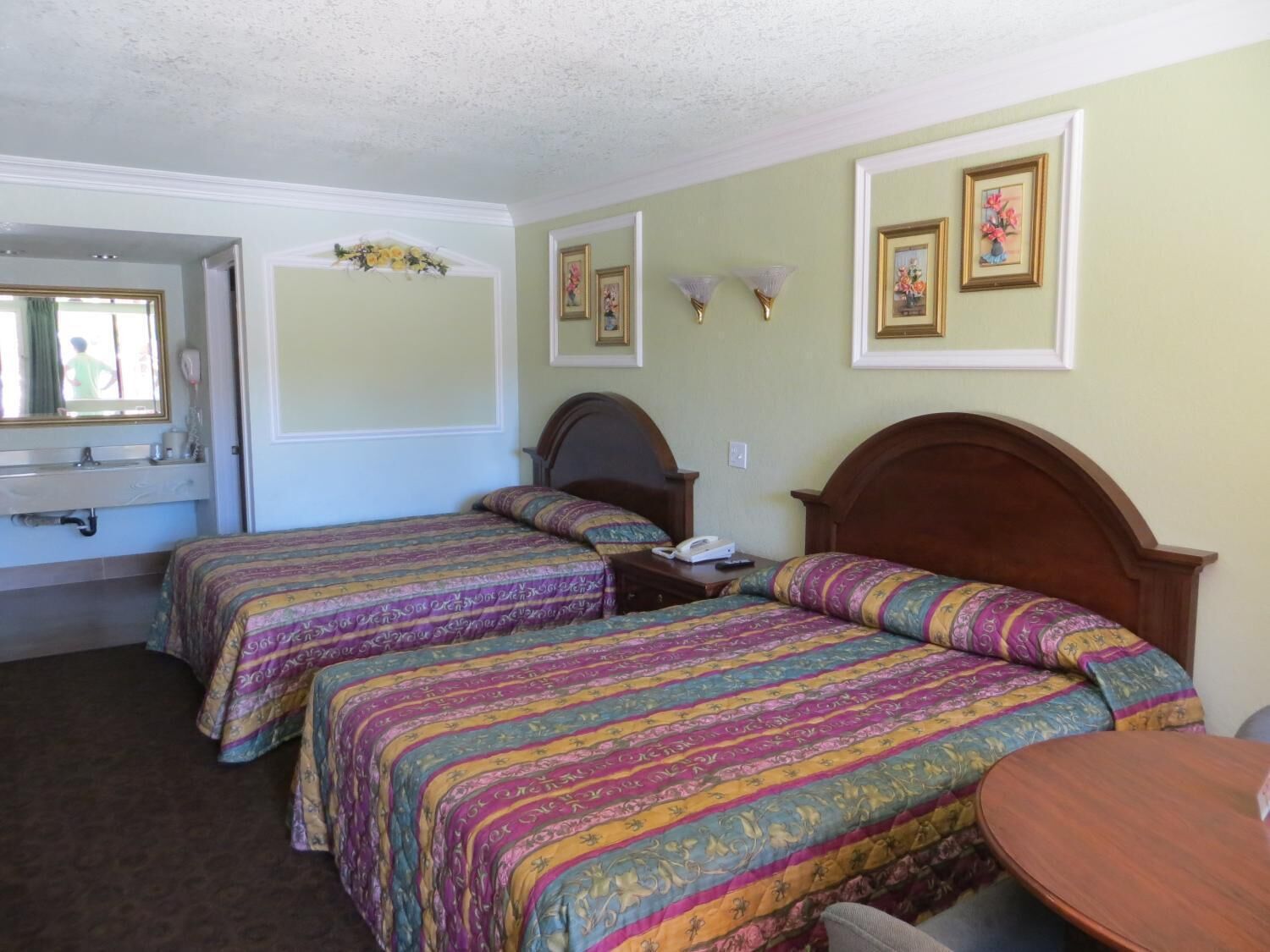 Habitación de hotel con dos camas, una mesita, un espejo y cuadros en la pared.