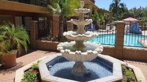 A multi-tiered fountain in a courtyard with a pool, surrounded by potted plants and a building with balconies. - Azusa INN Motel (La Puente)
