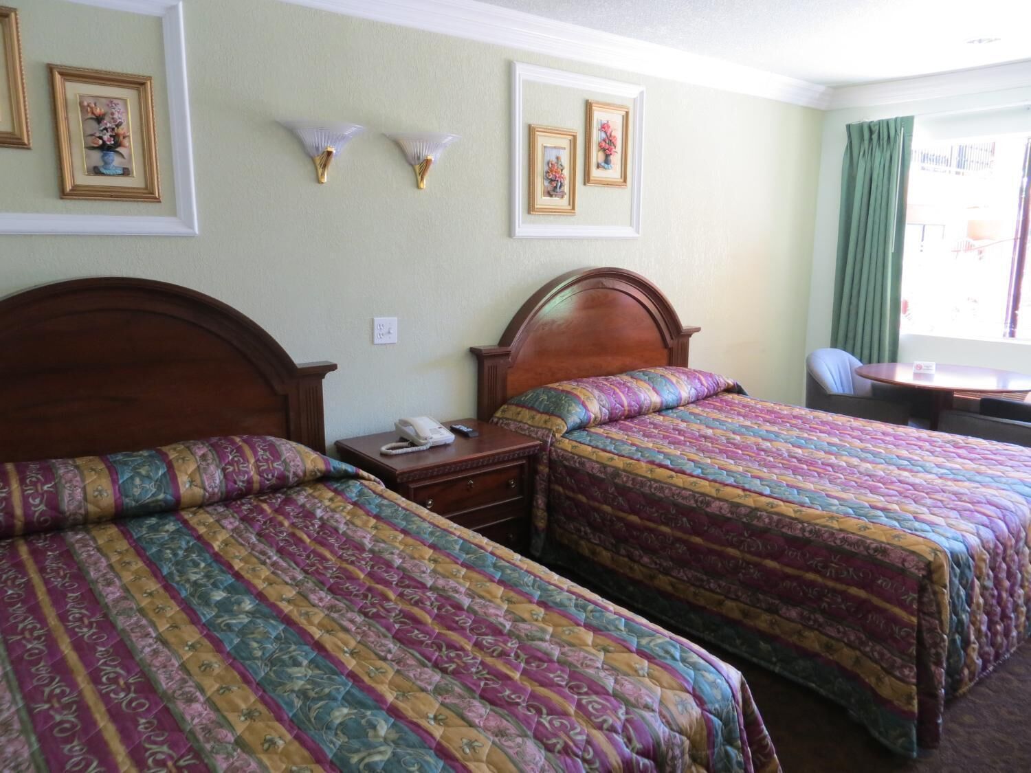 A hotel room with two beds, a desk, a chair, and a window with curtains.