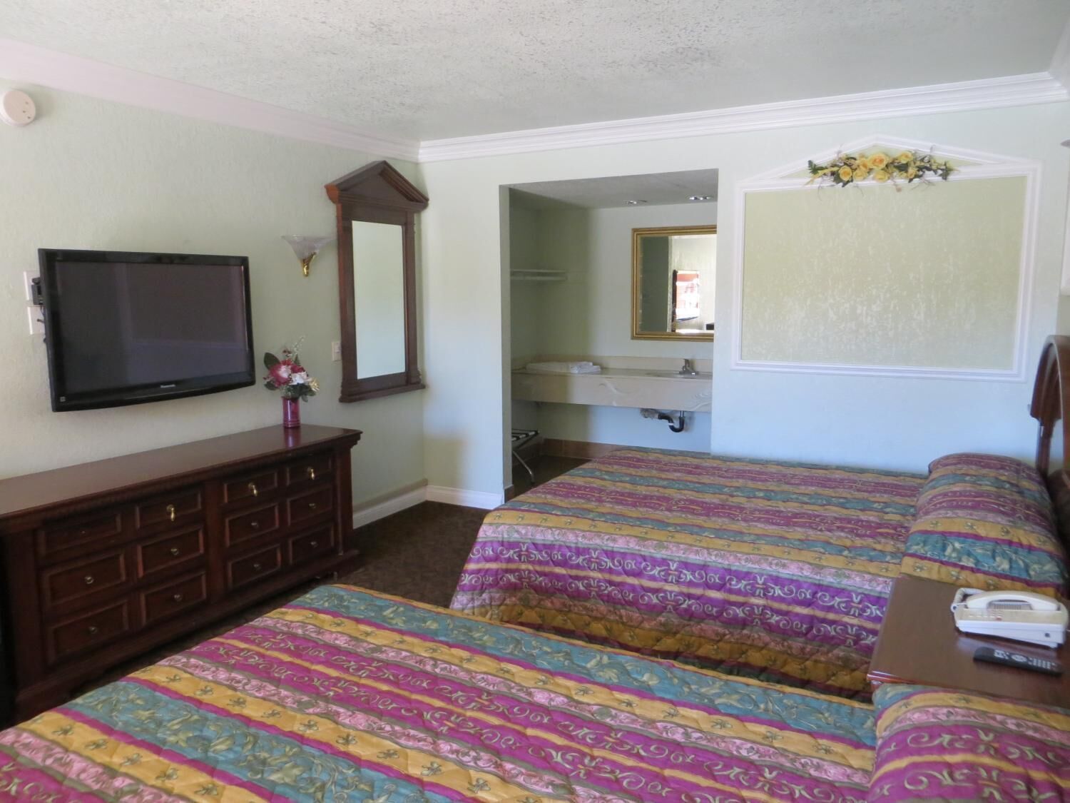 Habitación de hotel con dos camas, un aparador, un televisor, un espejo y un baño a la vista a través de una puerta abierta.