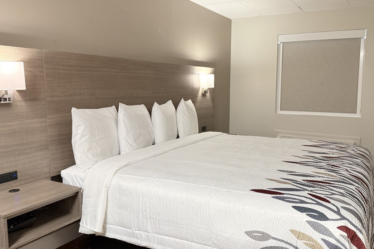 A neatly made bed with a patterned bedspread, a bedside table with a lamp, and a wall-mounted light fixture.