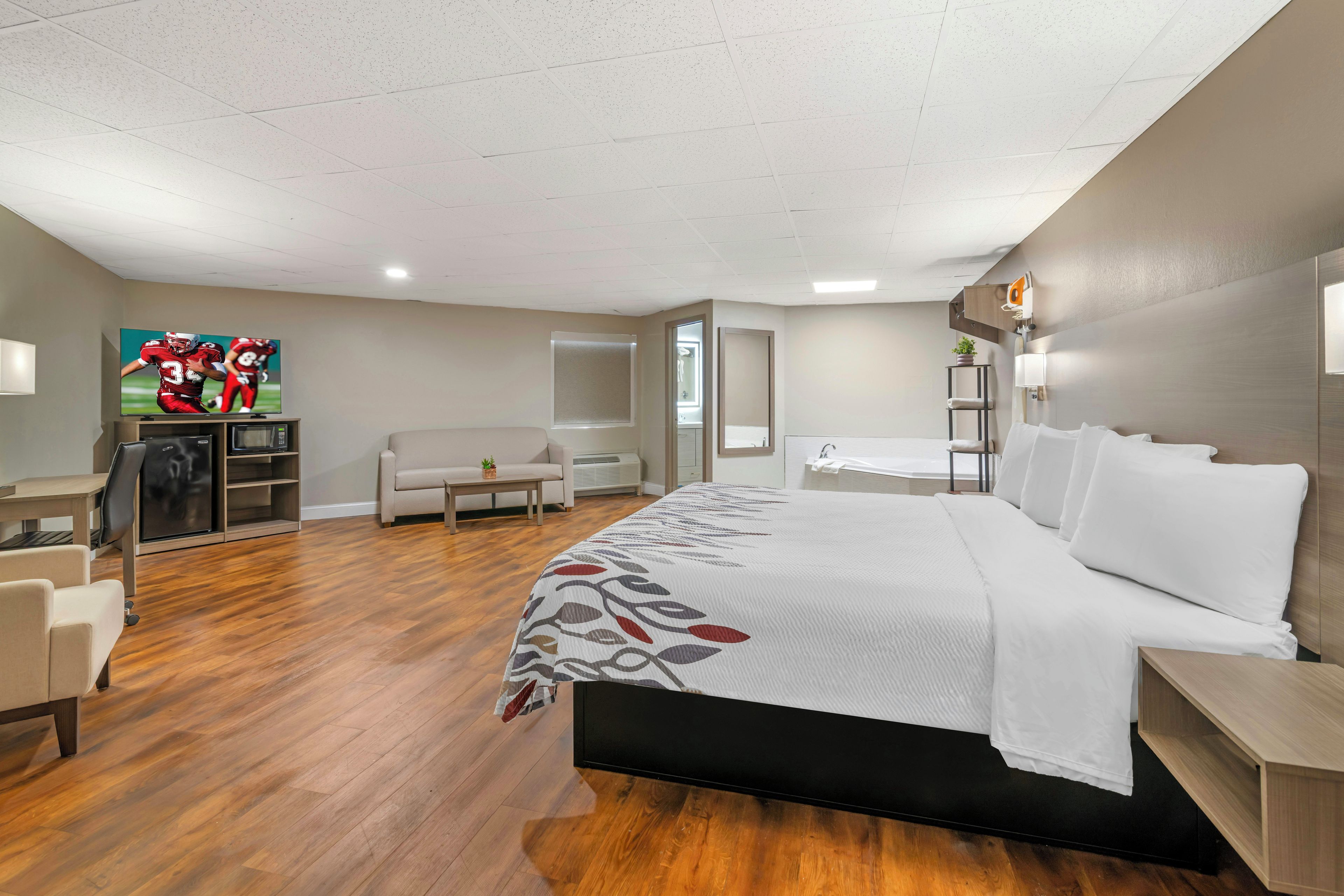 Quarto de hotel com cama, escrivaninha, cadeira, sofá, televisão e banheiro.