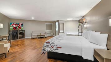 Quarto de hotel com cama, escrivaninha, cadeira, sofá, televisão e banheiro.