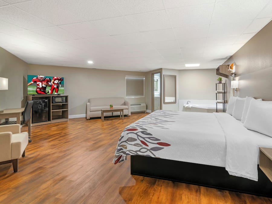 A hotel room with a bed, a desk, a chair, a sofa, a TV, and a bathroom.