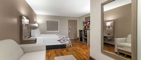 A hotel room with a bed, a sofa, a desk, a TV, and a large mirror.