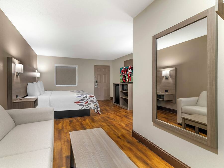 A hotel room with a bed, a sofa, a desk, a TV, and a large mirror.