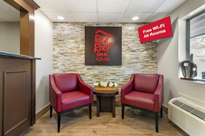 A Red Roof Suites hotel lobby with two leather chairs, a stone wall, and a sign indicating free Wi-Fi in all rooms.