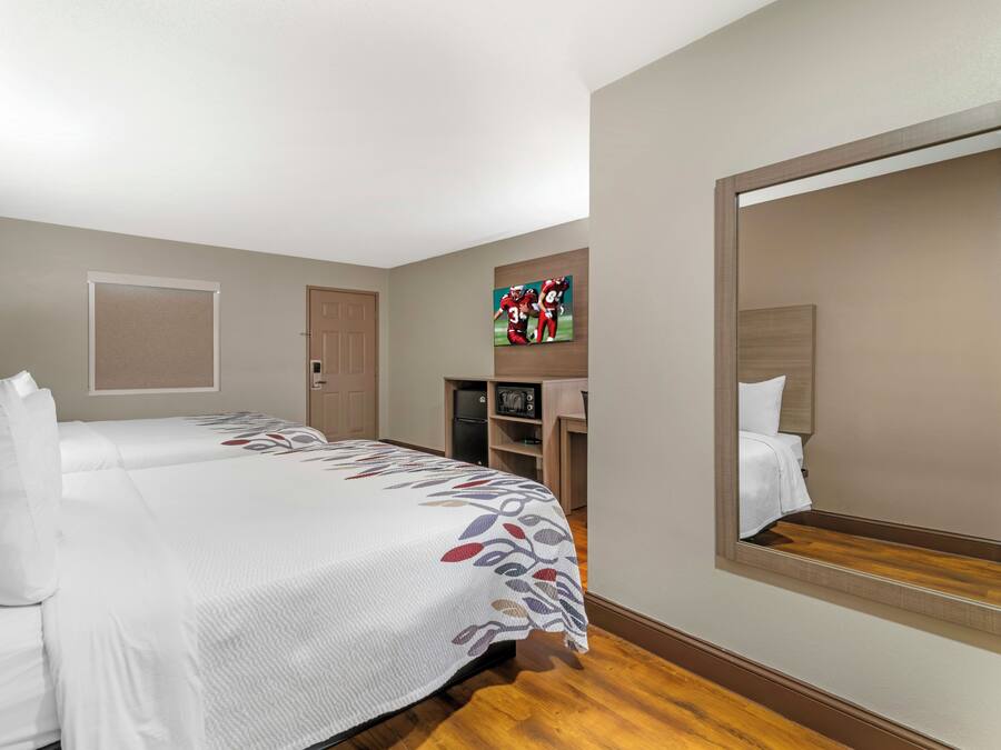 A hotel room with two beds, a large mirror, a television, and a small kitchenette.