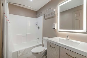 A modern bathroom with a bathtub, toilet, vanity, and a mirror. - Red Roof Inn & Suites Swansea (Swansea)