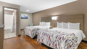 A hotel room with two beds, a wooden floor, a bathroom with a shower, and a painting on the wall.