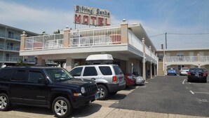 Een motel met een bord waarop 'Sittin' Sando Motel' staat en een parkeerplaats met verschillende voertuigen.