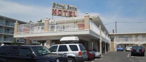 Un motel con un cartel que dice "Sittin' Sando Motel" y un estacionamiento con varios vehículos.