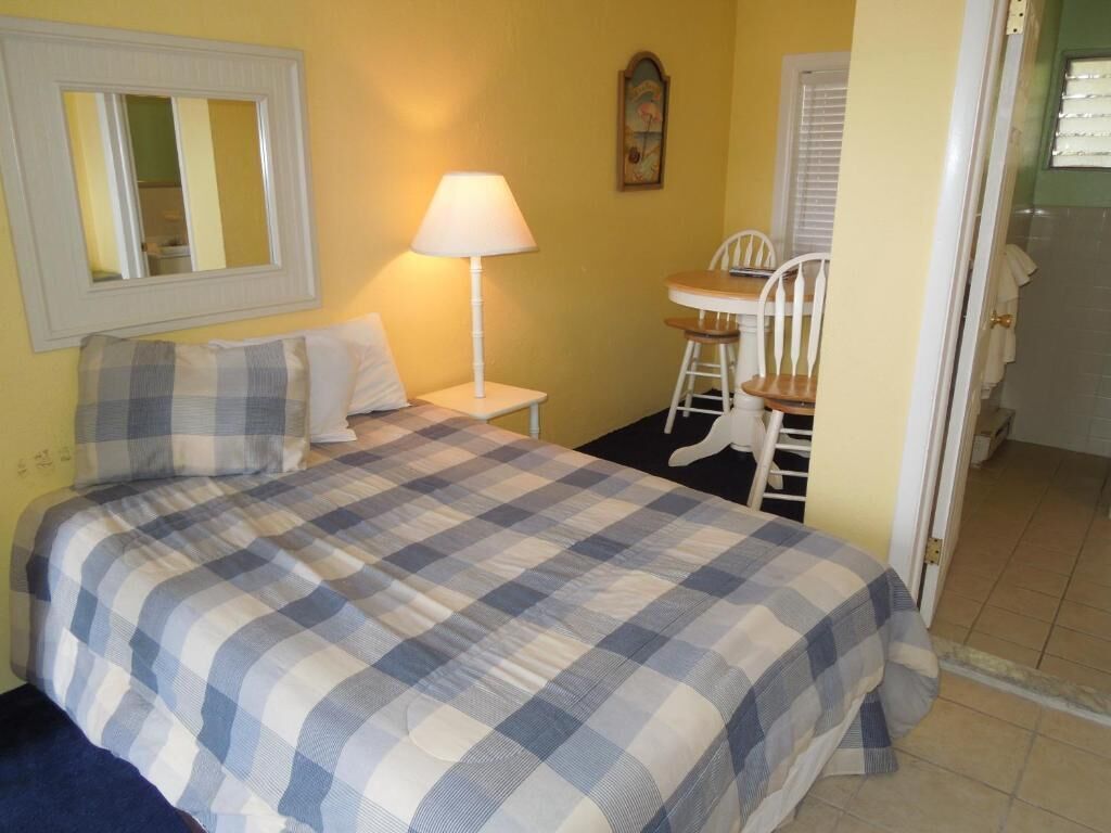 A bedroom with a bed, a bedside table with a lamp, a chair, and a small table.