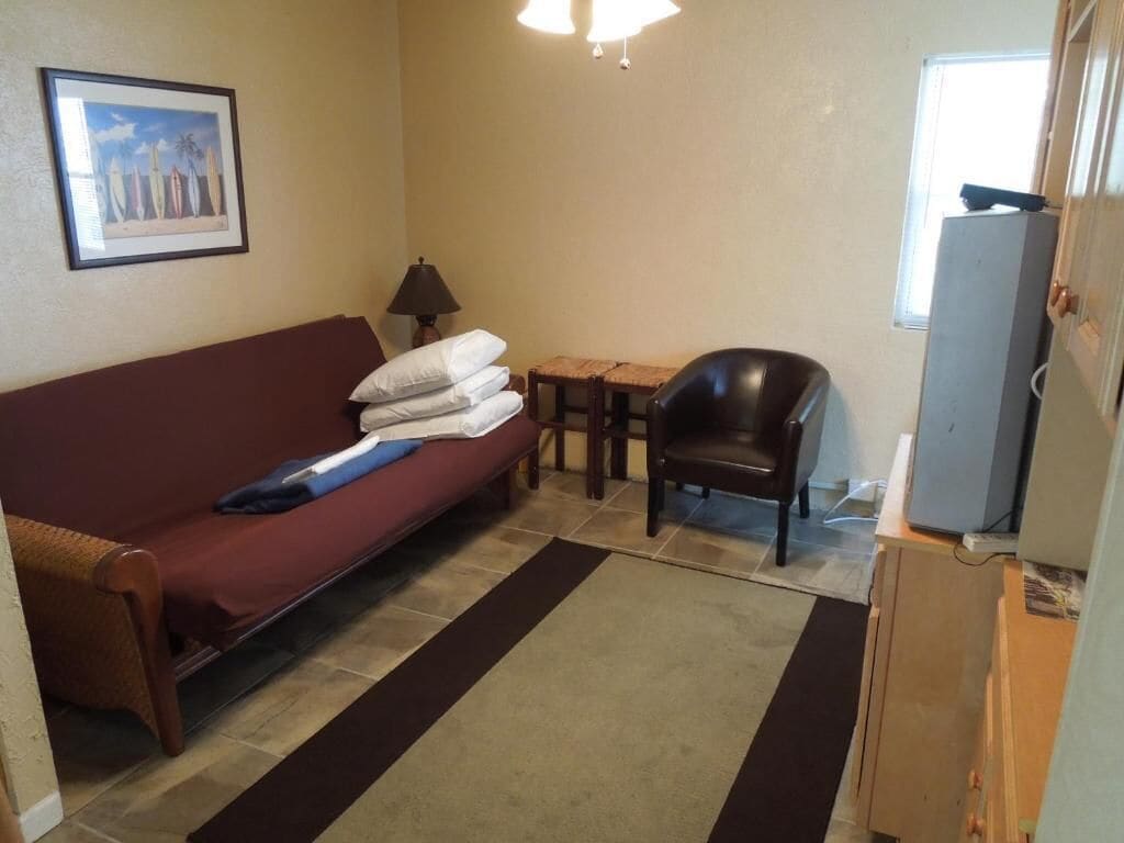 Une pièce avec un canapé rouge, une petite table en bois, une chaise noire, une lampe et un téléviseur posé sur un meuble en bois.