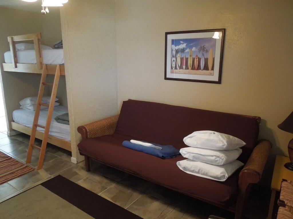 Een kamer met een stapelbed, een slaapbank, een lijst met een foto aan de muur, en een lamp.