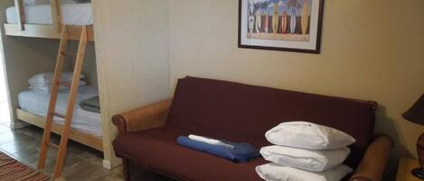 A room with a bunk bed, a sofa, a framed picture on the wall, and a lamp.