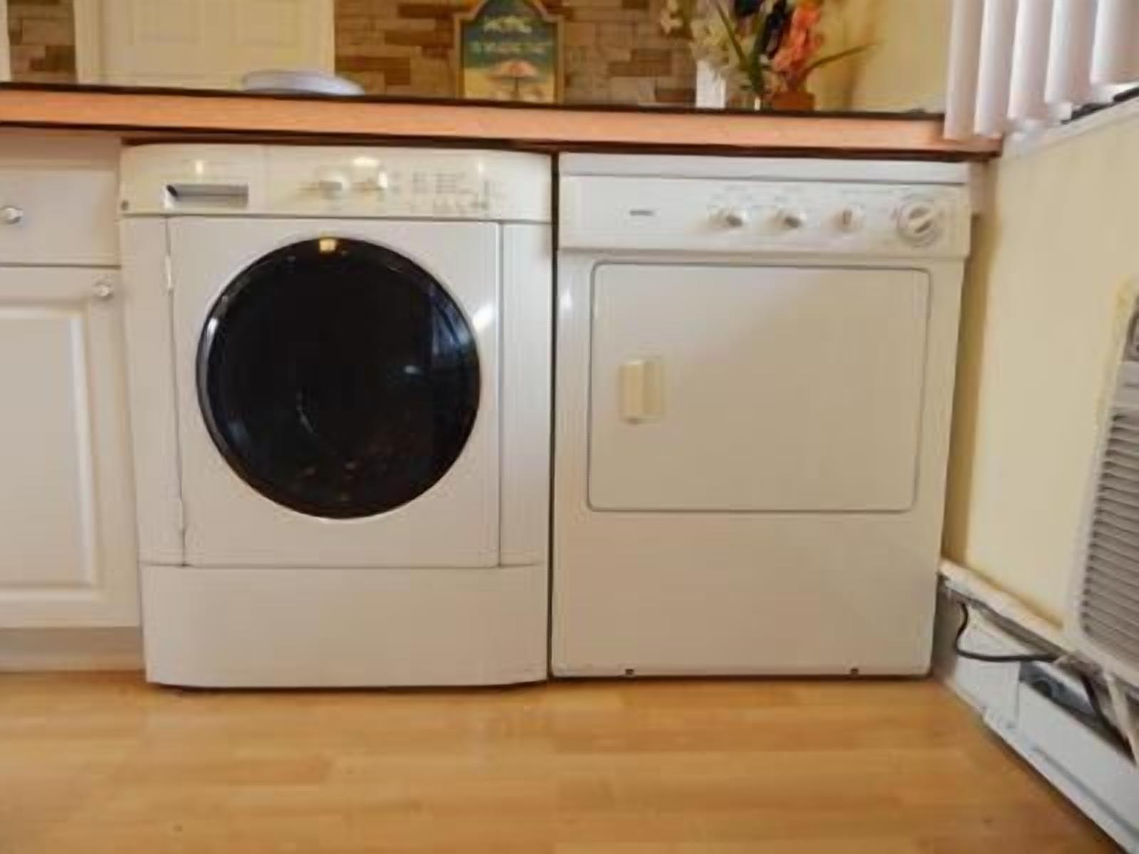 Un lavadero pequeño y blanco, con lavadora y secadora, suelo de madera y salpicadero de azulejos.
